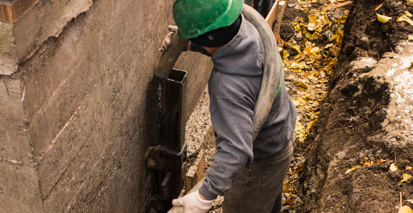 Travailleur coulant du ciment dans des pieux d’acier pour renforcer ou remettre la fondation à niveau.